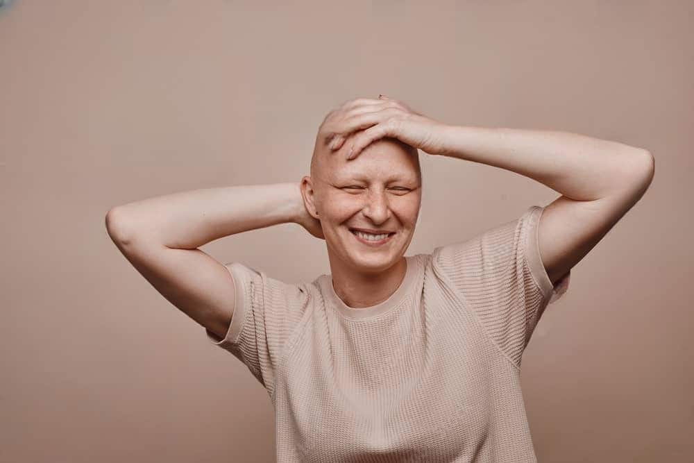 A bald woman touching her head